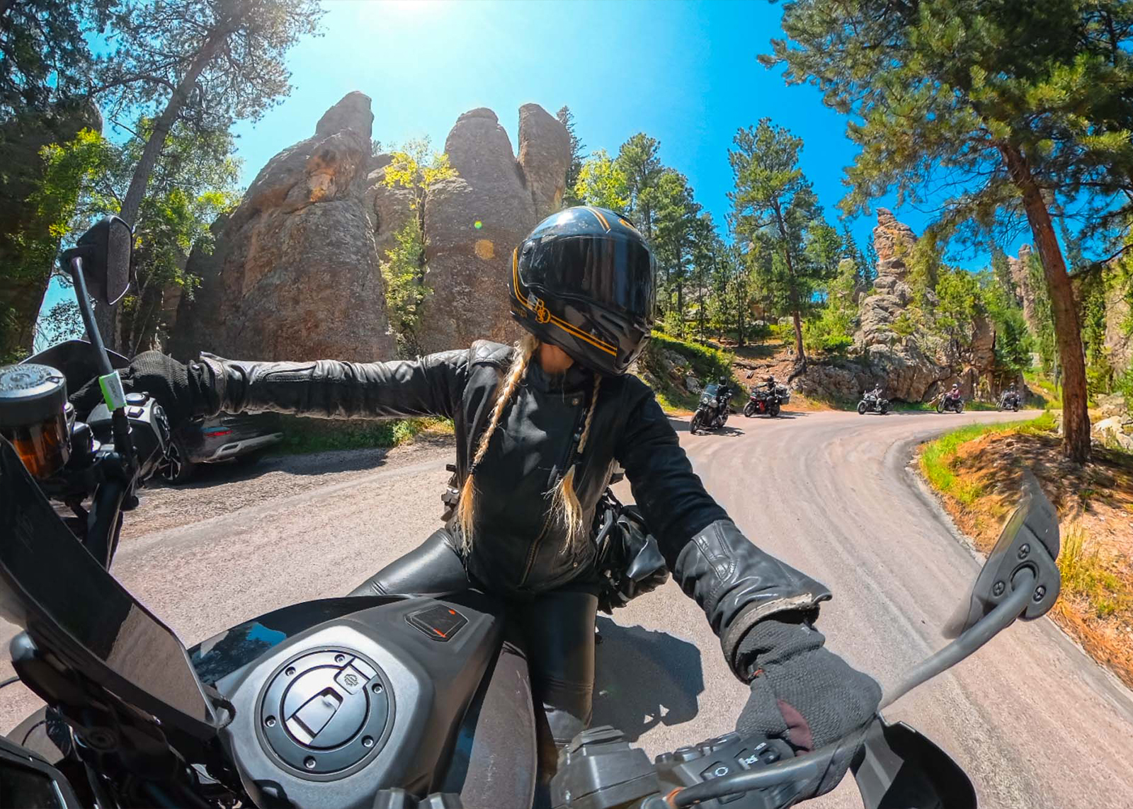 Handlebar-mounted camera looks back at rider leading a group through a winding forest road with rocks.