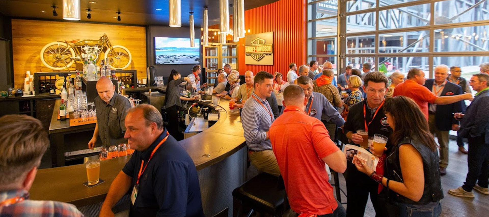 Crowd of people gathered around bar counter inside Harley‑Davidson themed venue