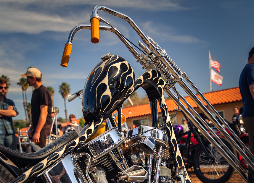 Tall‑fork chopper with flame paint and chrome parts showcased at a crowded outdoor bike event