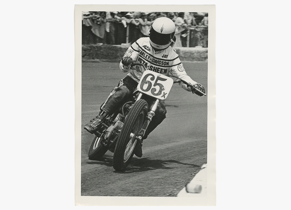 Black-and-white photo of Jay Springsteen leaning a Harley-Davidson motorcycle through a turn in 1975