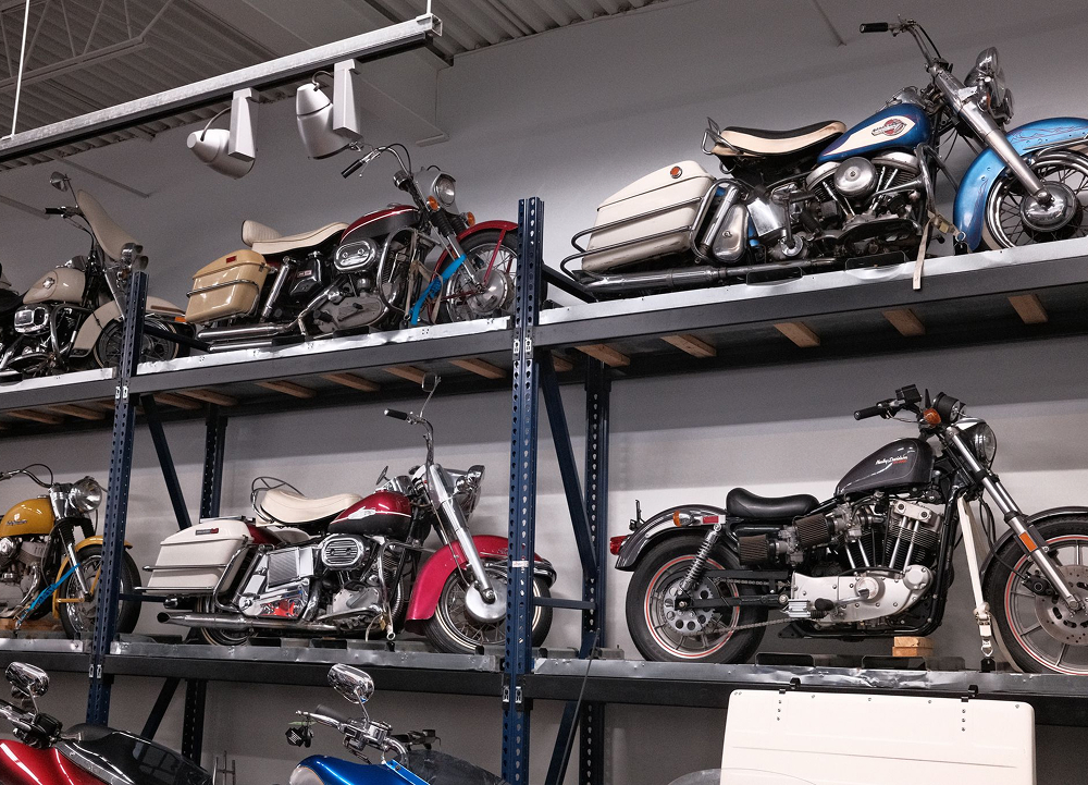 Rows of vintage H-D motorcycles stored on metal shelving inside organized service department
