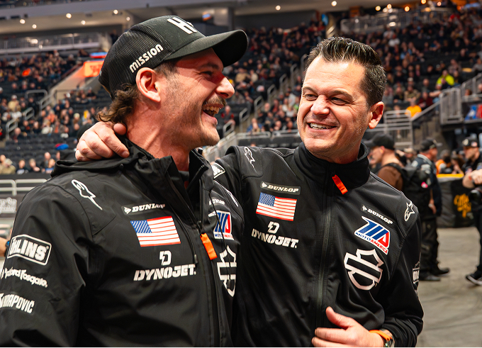 Two Harley-Davidson Racing team members in branded racing jackets stand together on the arena floor