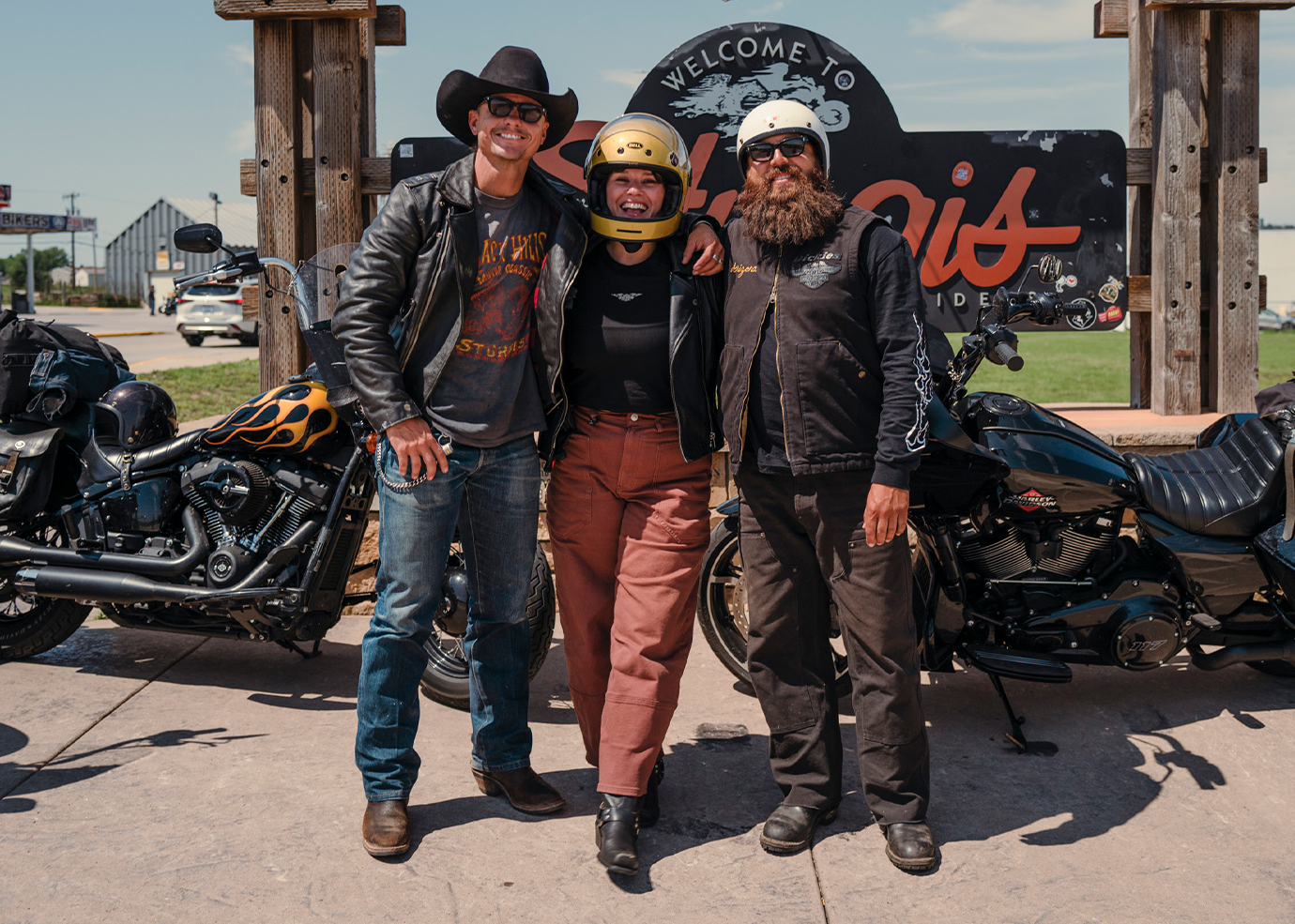 3 riders smiling in front of sturgis sign