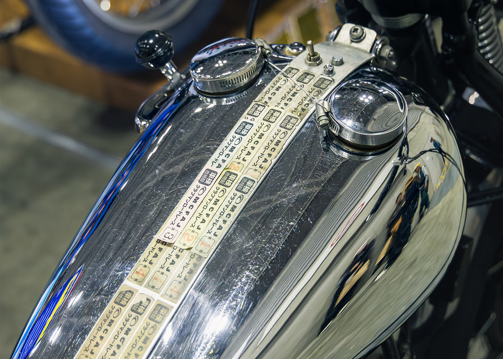 Close-up of a polished motorcycle fuel tank featuring two chrome caps and a strip with Japanese characters
