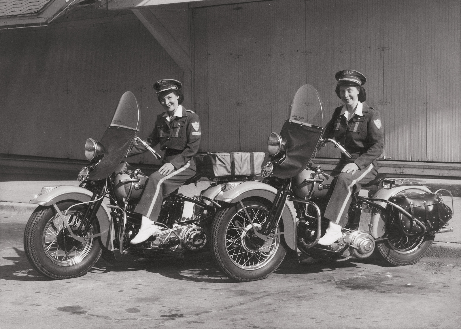 A vintage photo of two Motor Maids sitting on their motorcycles in full uniforms.