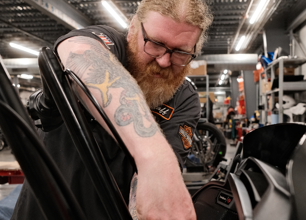 Technician working on a Harley-Davidson motorcycle inside a service bay with workshop equipment