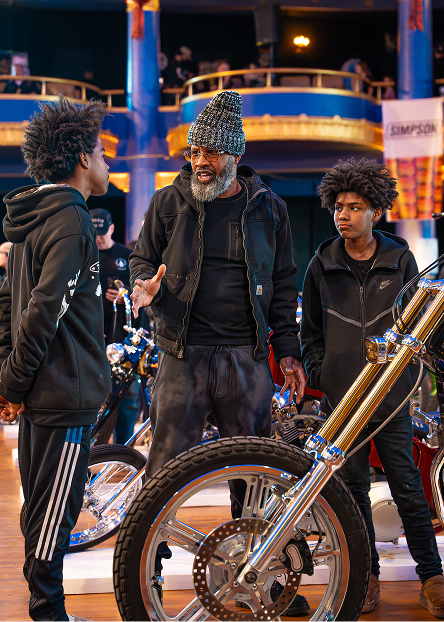 A father with his two sons stand beside a chrome‑accented custom motorcycle at Mama Tried
