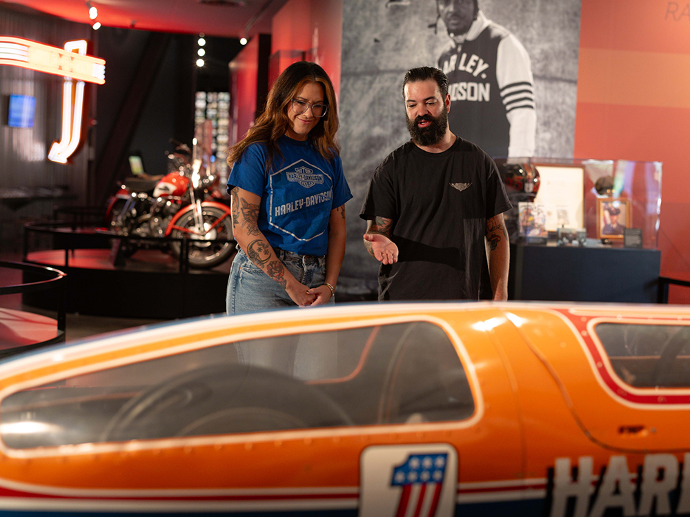 Visitors observing orange racing motorcycle display inside museum exhibit