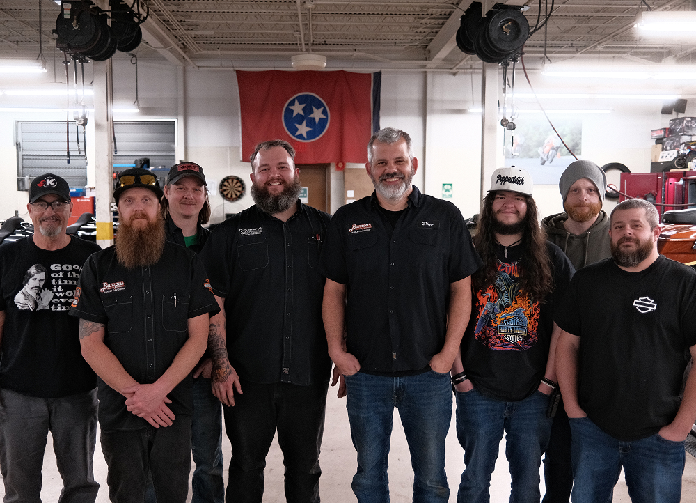 The service team at Bumpus Harley-Davidson standing together with tools, banners, and motorcycles