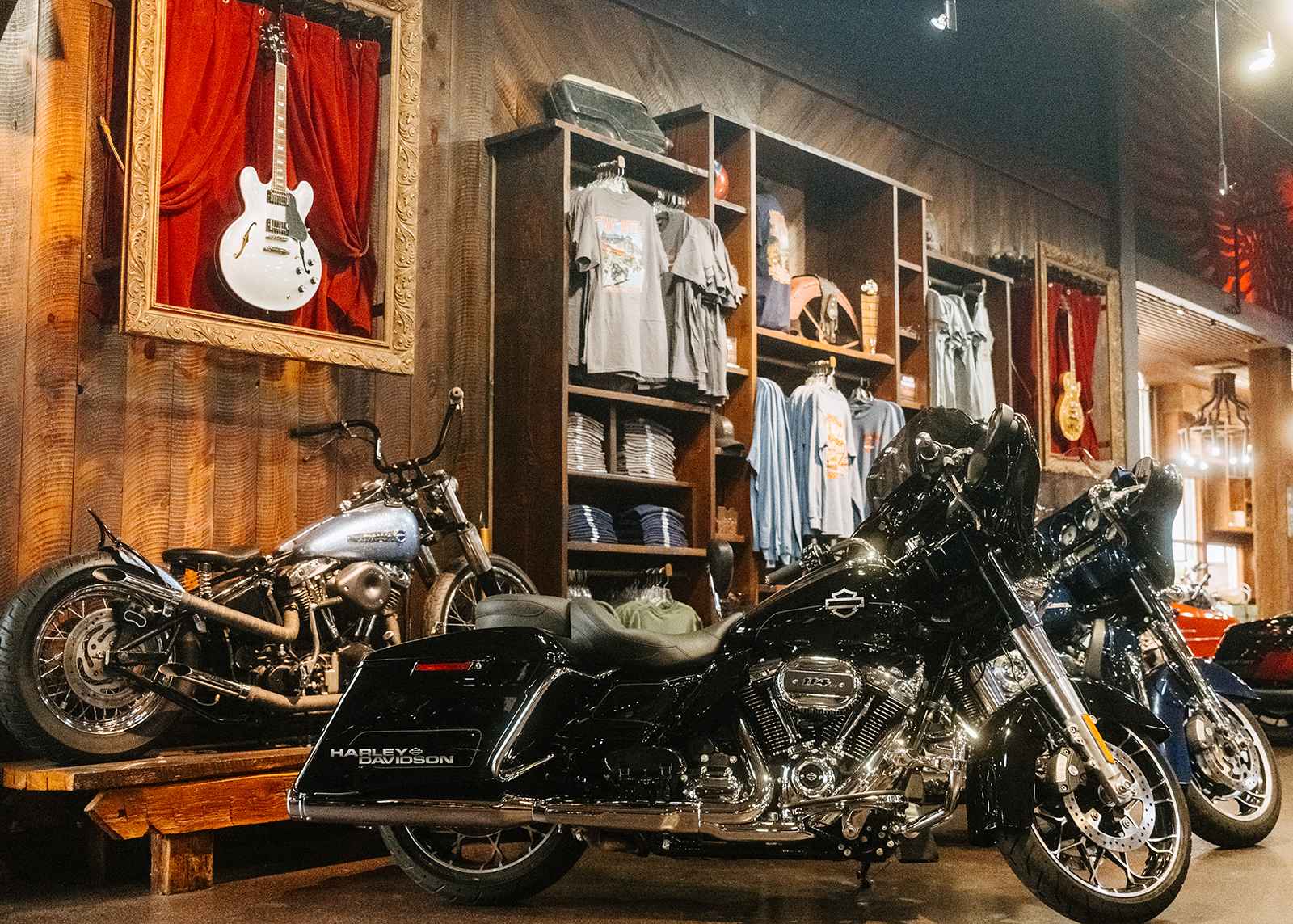 Two bikes in the wood-paneled showroom of Smokey Mountain Harley-Davidson dealership, with guitars displayed as decoration in the background.