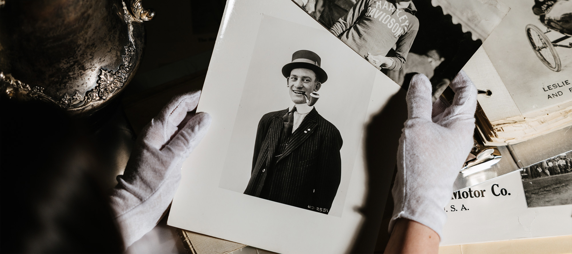 An archivist holds two photos of Red: one in a dapper suit and hat with his pipe, the other with disheveled hair in a Harley shirt.