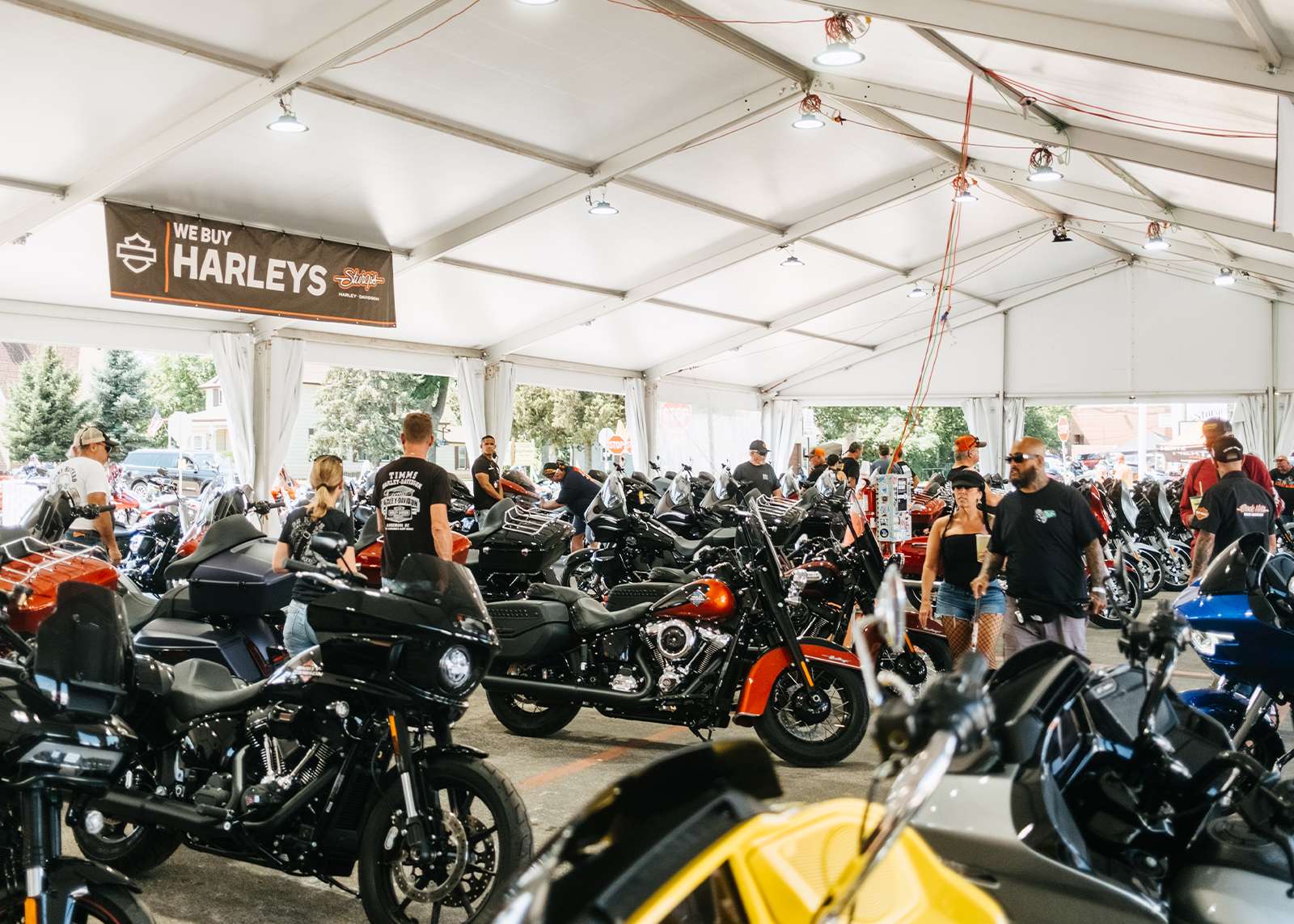 People browse rows of Harley-Davidson motorcycles under a large event tent at Sturgis Harley-Davidson Dealership.