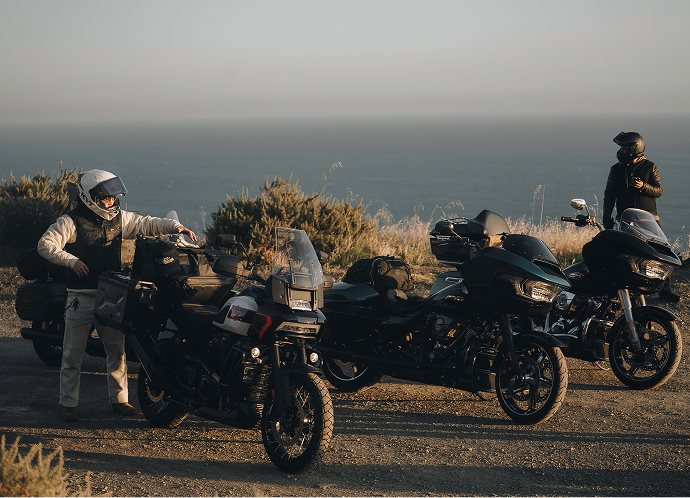 Three motorcycles parked at a coastal overlook with riders nearby and ocean horizon stretching into the distance