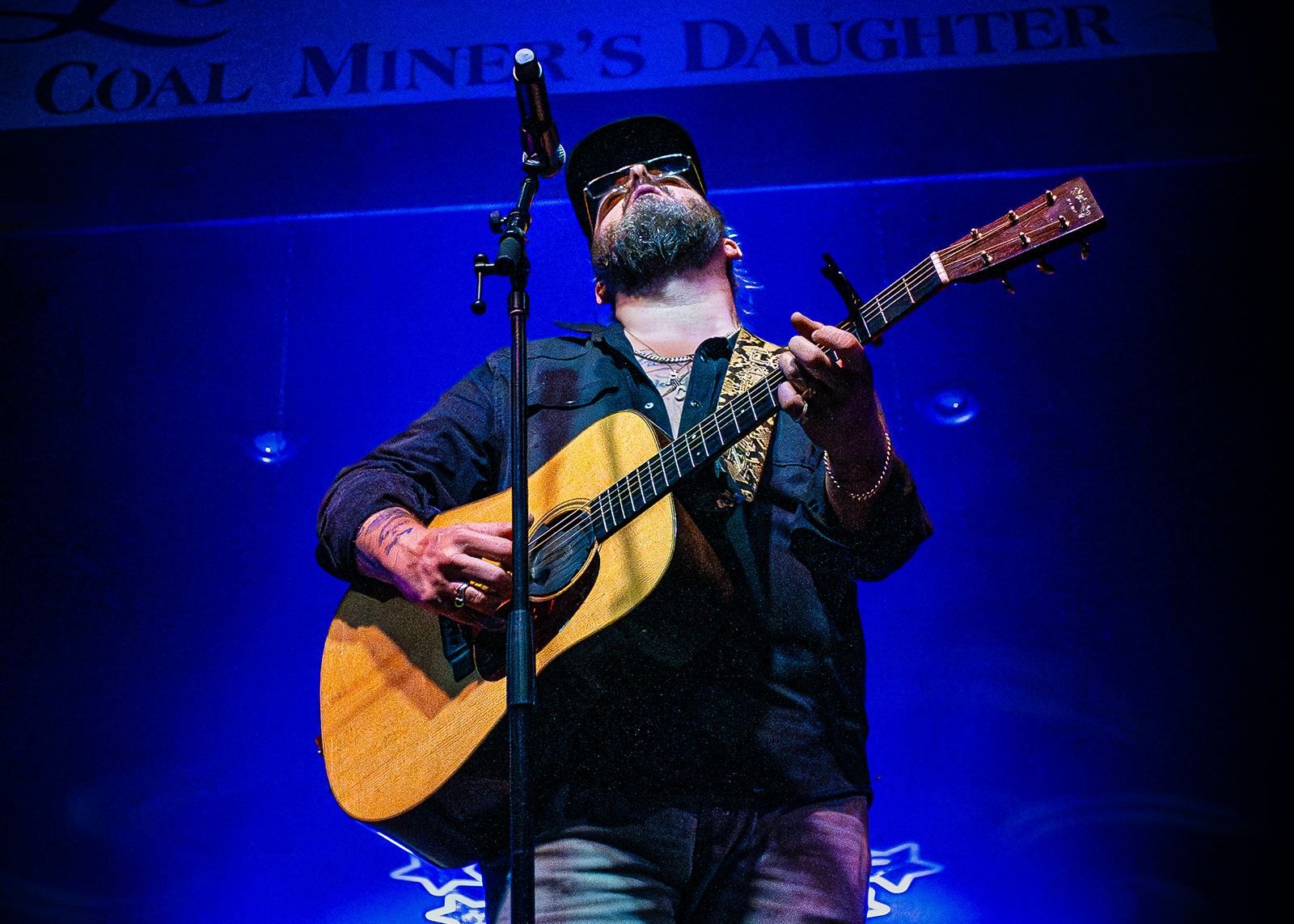 A singer with his guitar plays on stage bathed in blue light.