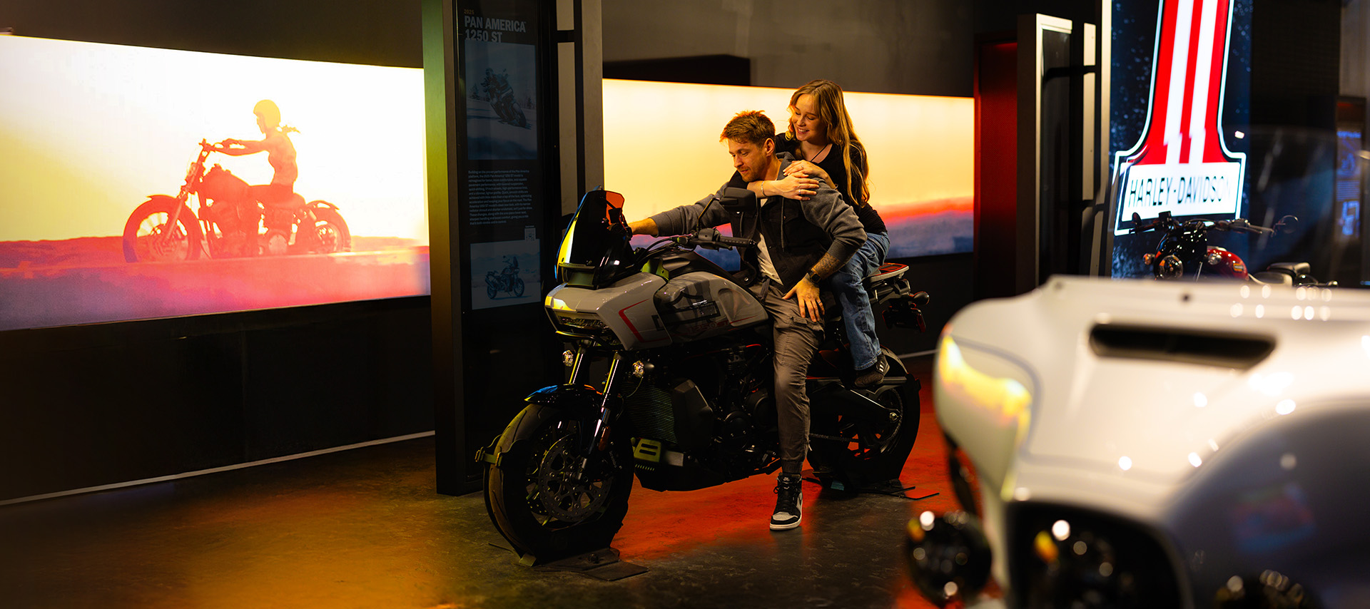 Two visitors sitting on motorcycle inside museum exhibit