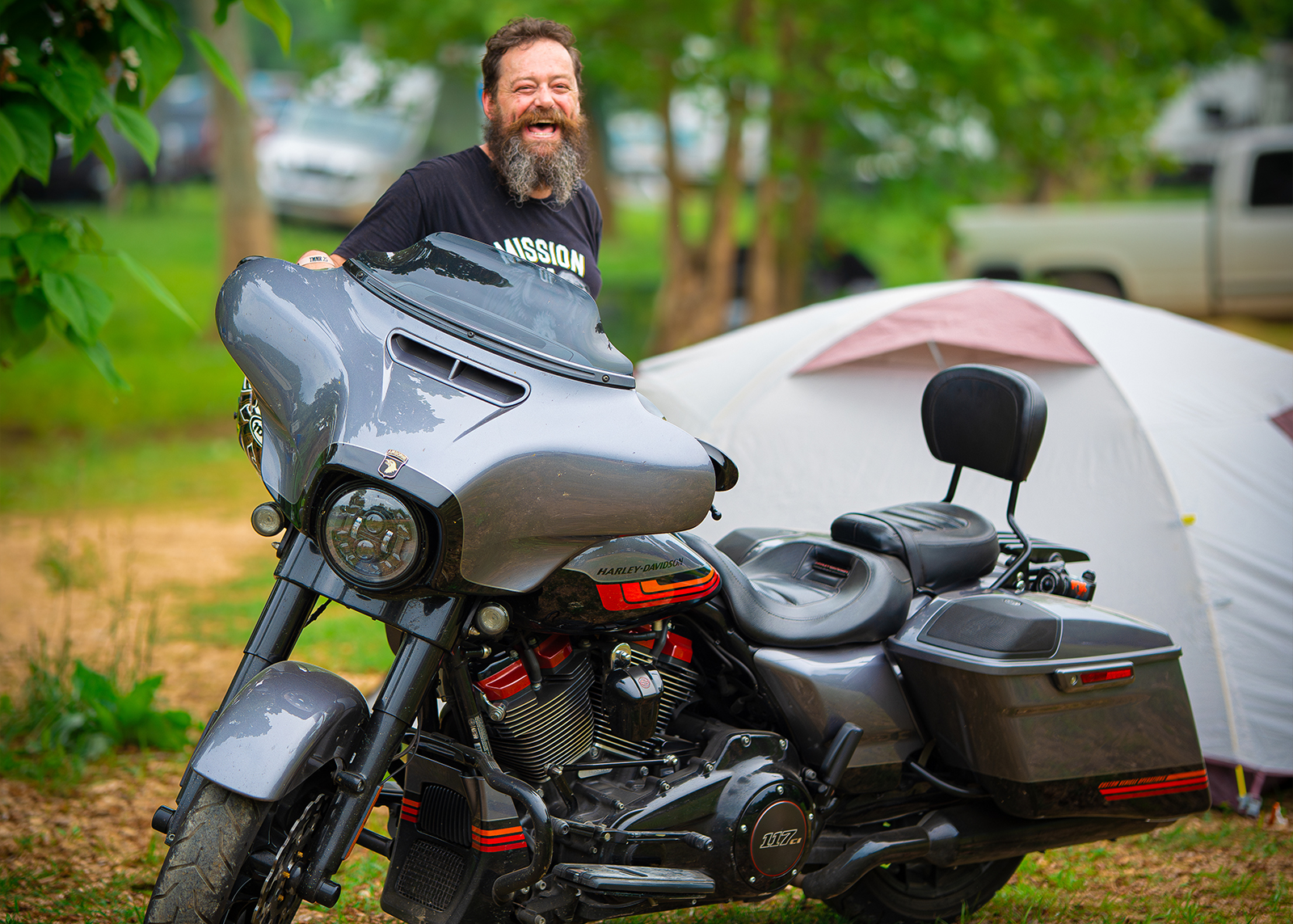 A man smiles standing with his tent and silver Harley.