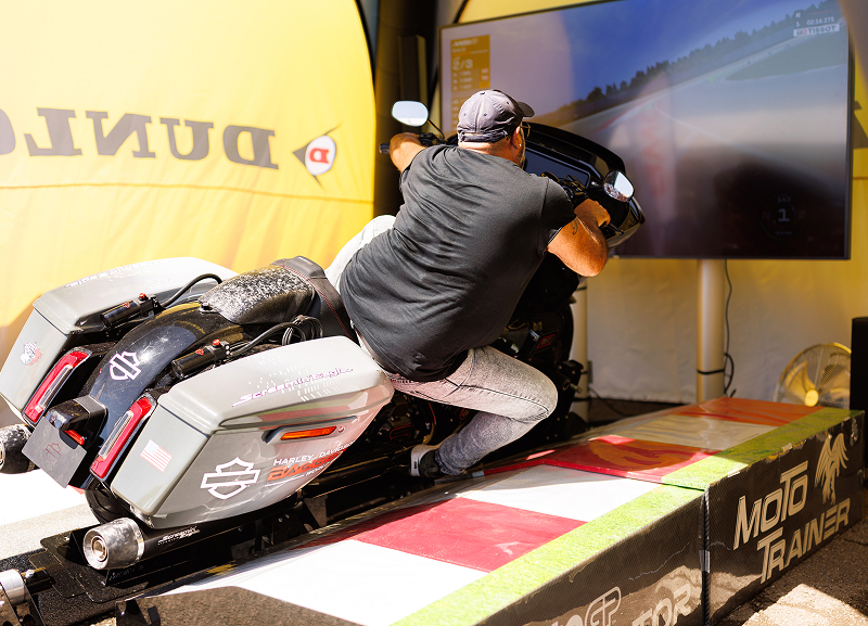 Person rides a Harley-Davidson touring motorcycle on a simulator, racing a virtual track at an event display