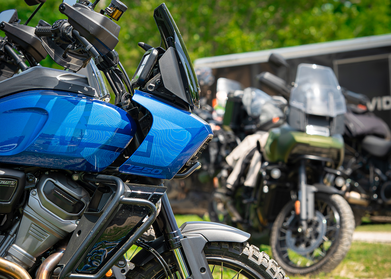 A side profile of a blue Pan America, with a green Pan America out of focus in the background.