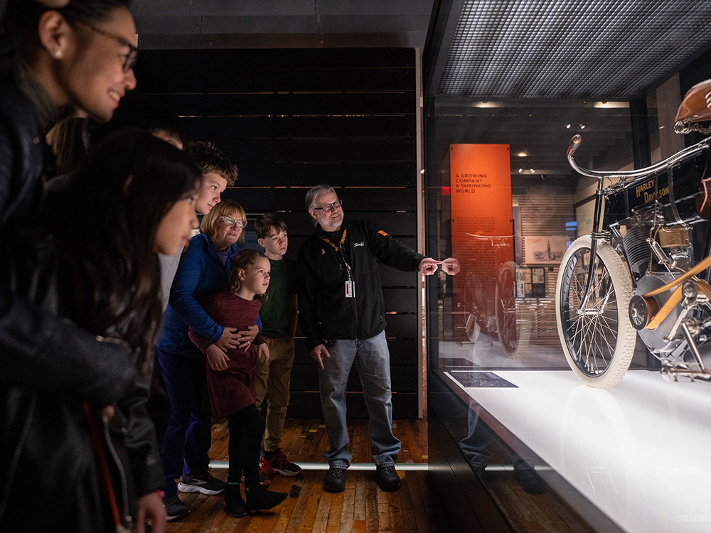 Guide explaining vintage motorcycle display to group of visitors in museum