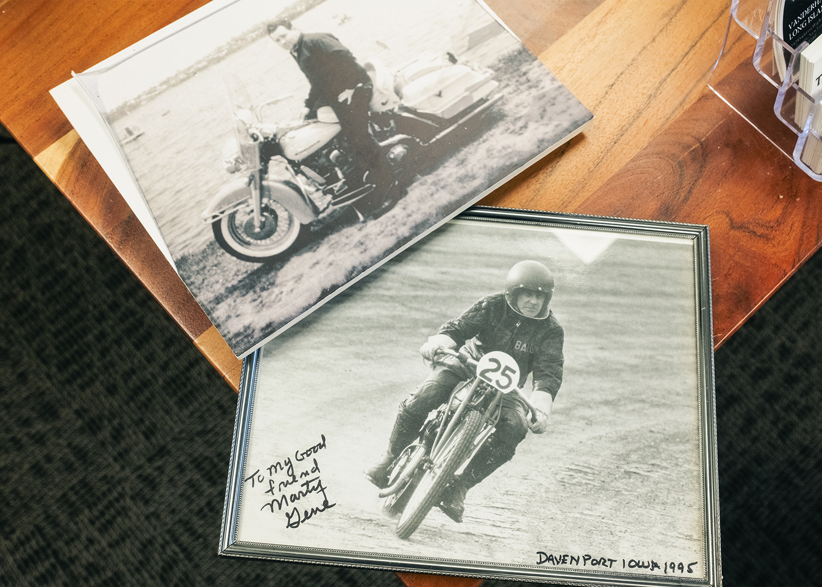 Framed vintage motorcycle photos with signatures sitting on a desk.