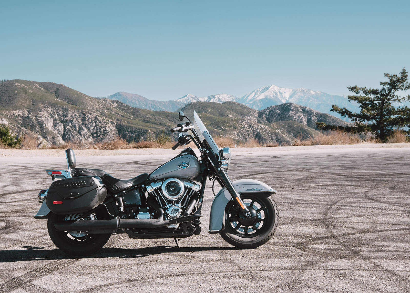 A Harley-Davidson Heritage Classic motorcycle parked roadside with distant snow capped peaks in the background