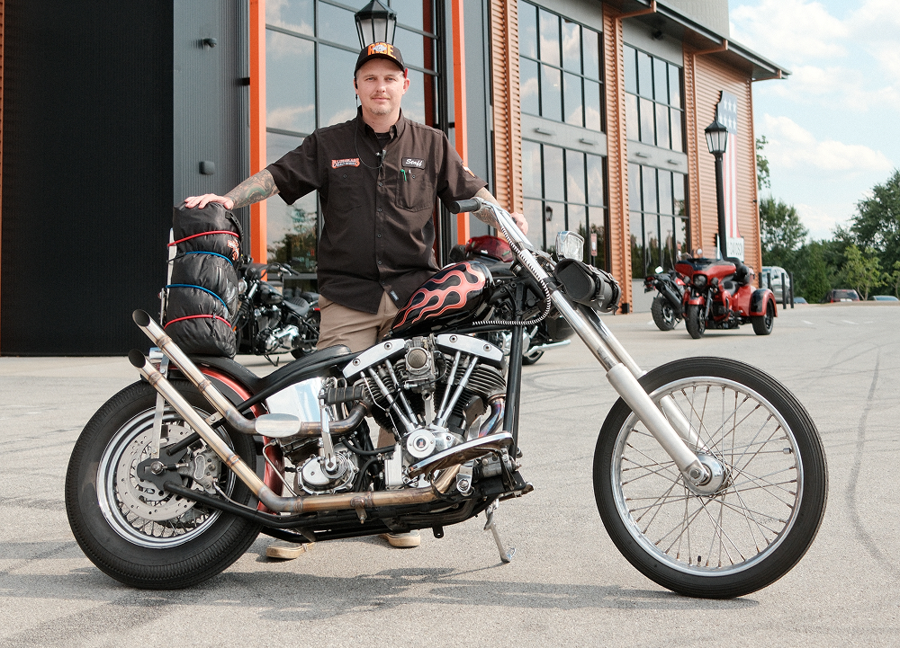 Custom black Harley-Davidson chopper with flame graphics and rider standing outside dealership entrance