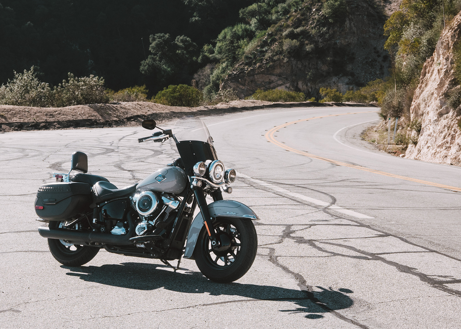 Side view of a Harley-Davidson Heritage Classic motorcycle parked roadside surrounded by steep cliffs and green foliage