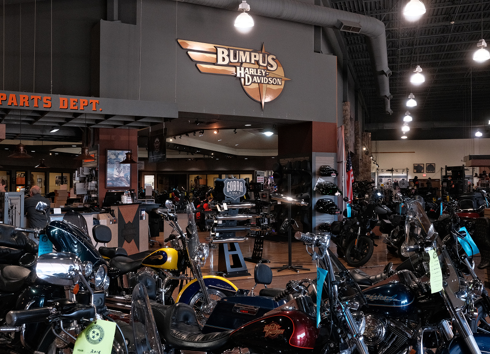 Interior of Bumpus Harley-Davidson showroom filled with motorcycles, parts displays, and branded signage overhead