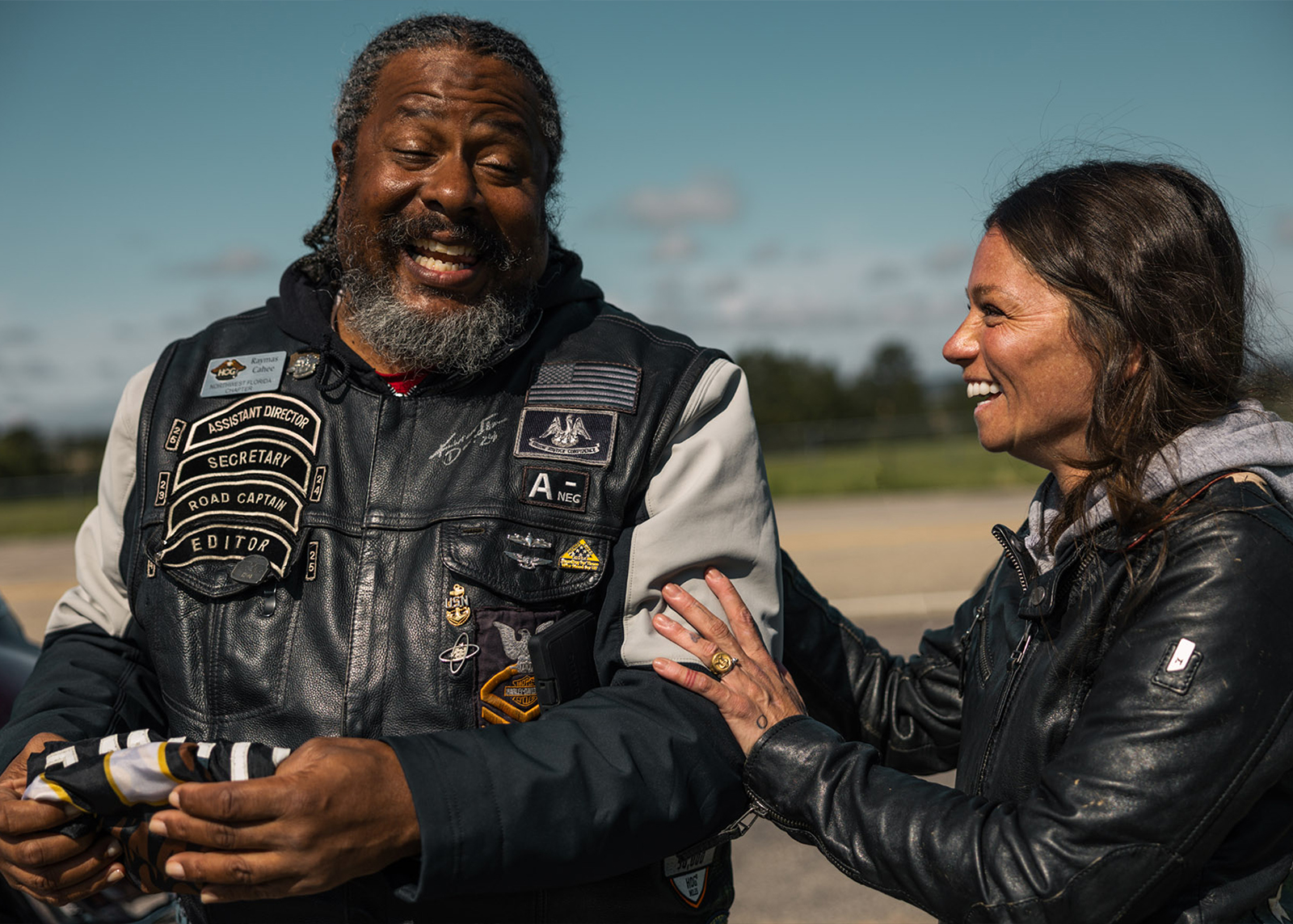 Two H.O.G. members in patch-covered vests standing outdoors and laughing together
