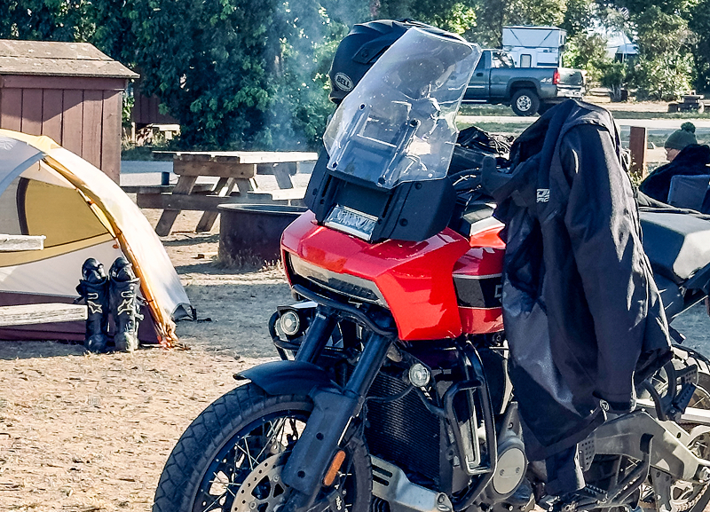 Red H-D Pan America motorcycle at campsite with tent, gear, and riding jacket draped over seat
