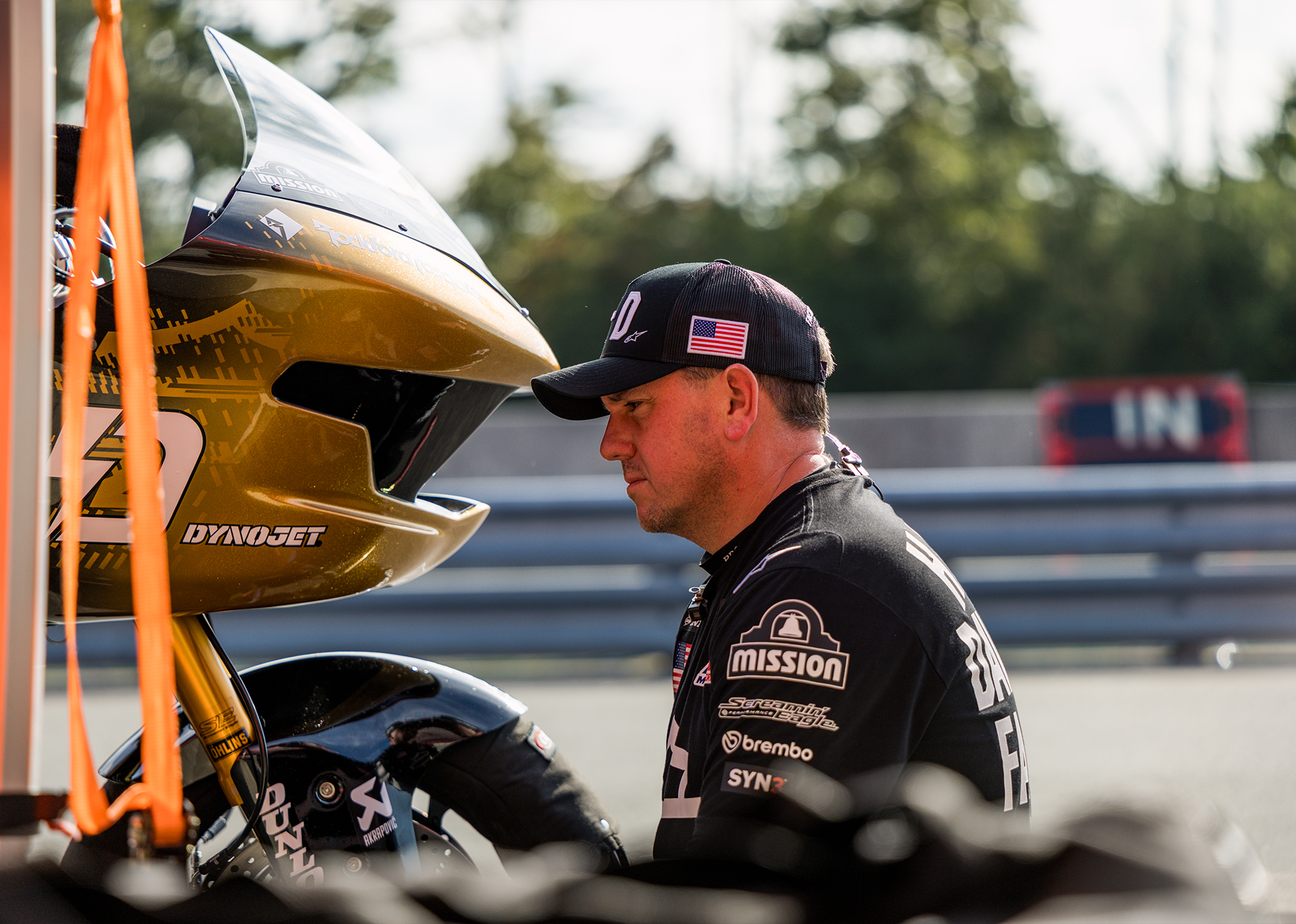 Harley-Davidson Factory Racing Chief Race Mechanic Dave Hopkinson sits thoughtfully in a race garage next to a gold motorcycle.