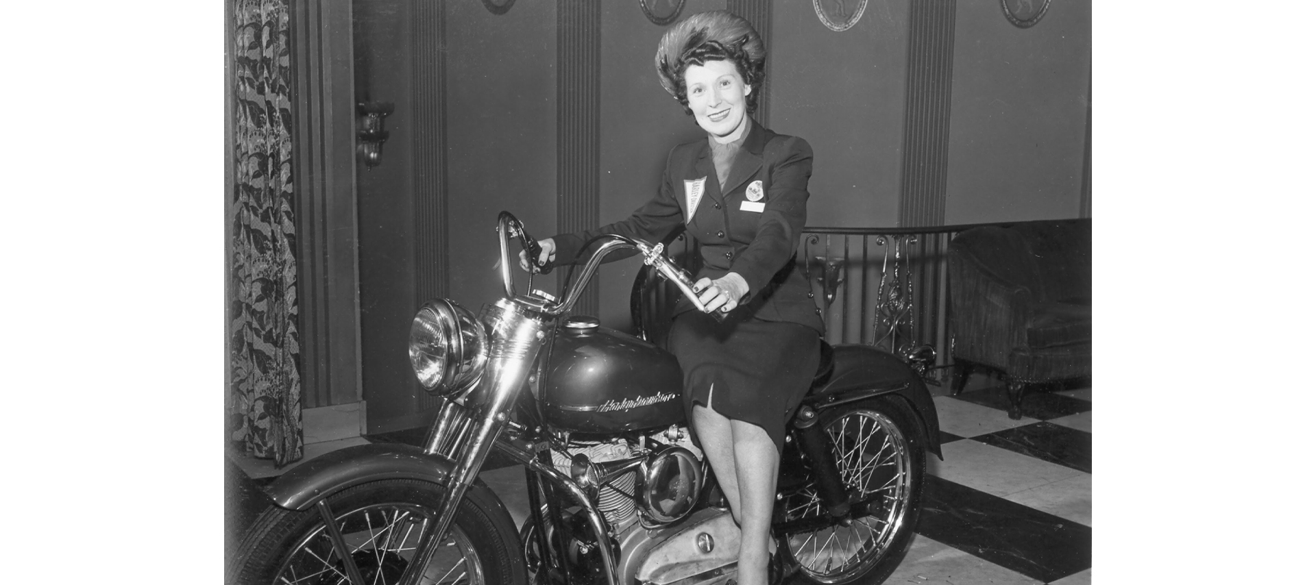 A woman sits side-saddle on a parked motorcycle indoors 