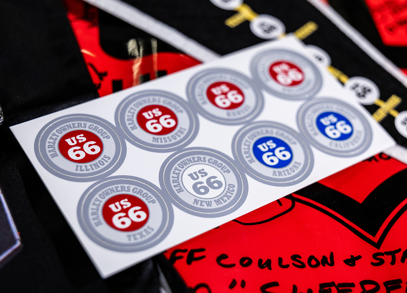 Sheet of 2010 Route 66 themed stickers laid over a signed red HOG banner with handwritten notes