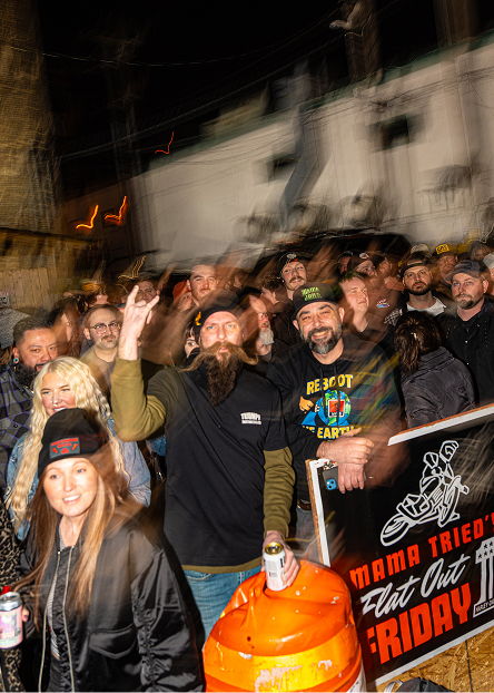 Crowd gathered behind a barricade cheering near event signage and orange safety barrels