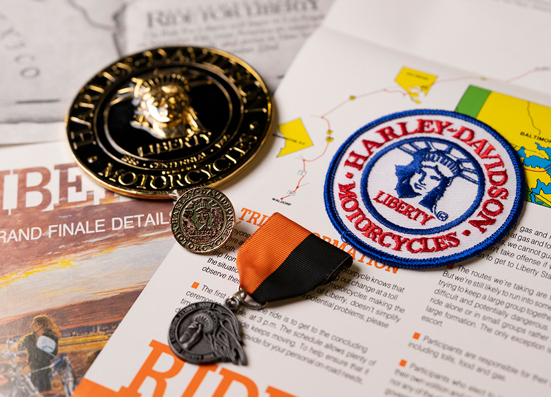 Harley-Davidson liberty memorabilia with medals, patch, and magazine pages arranged on a tabletop
