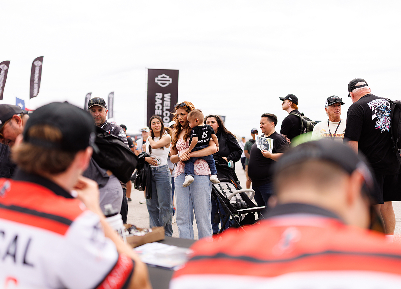 Crowd gathers around Harley-Davidson racers during a fan meet-and-greet at a motorcycle racing event
