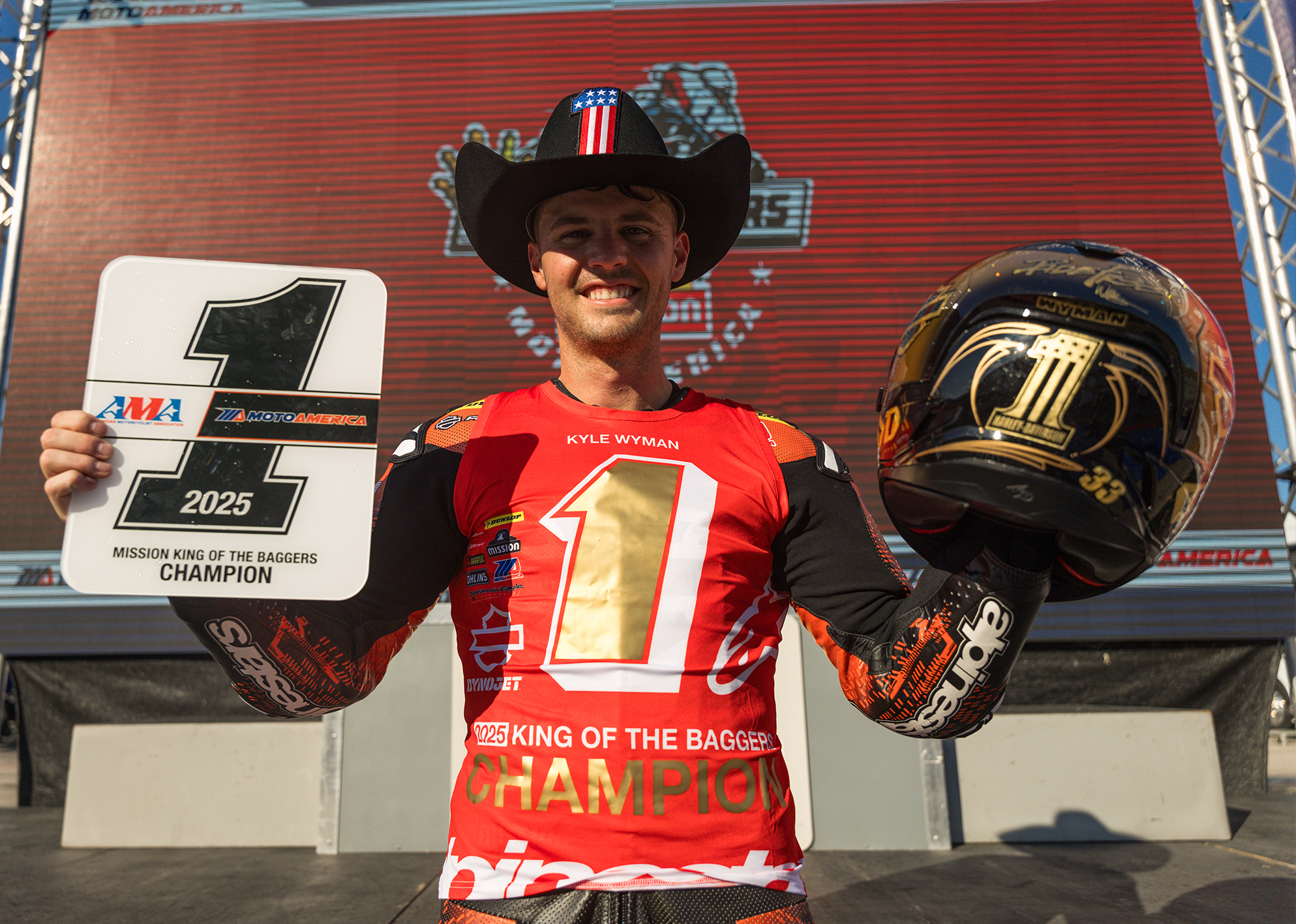 Kyle Wyman poses in a cowboy hat with the number one plate in one hand and a custom gold helmet in the other.
