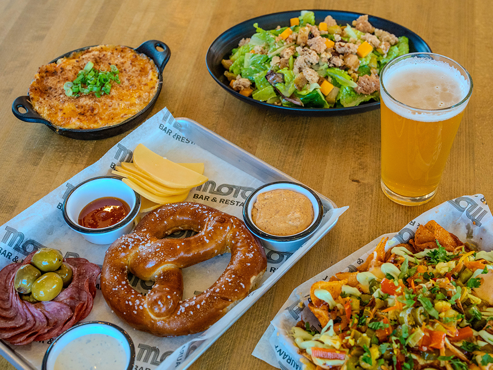 Assorted bar food with pretzel, nachos, dips, salad, and beer on table