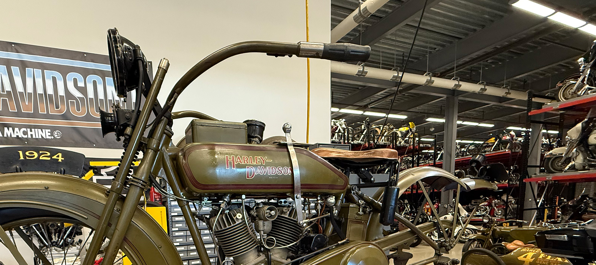 Antique Harley-Davidson motorcycle displayed in workshop with multiple bikes in background