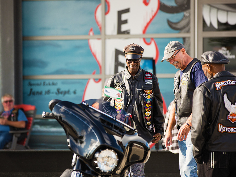 two men standing next to a Harley motorcycle