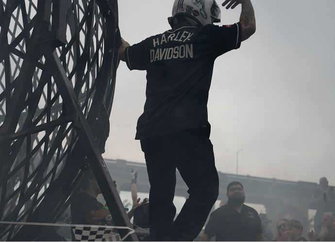 Stunt rider wearing a Harley-Davidson shirt and helmet standing beside the metal globe of death structure