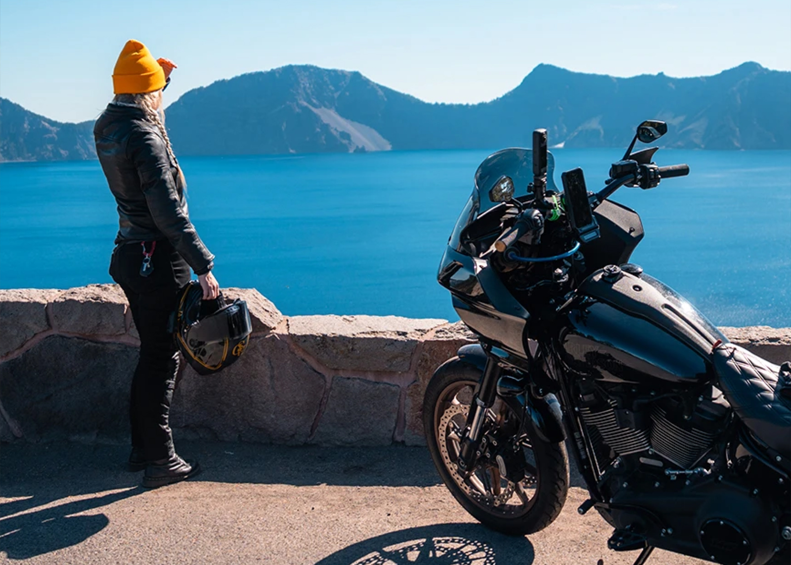 rider overlooks crater lake oregon standing next to parked hd lowrider