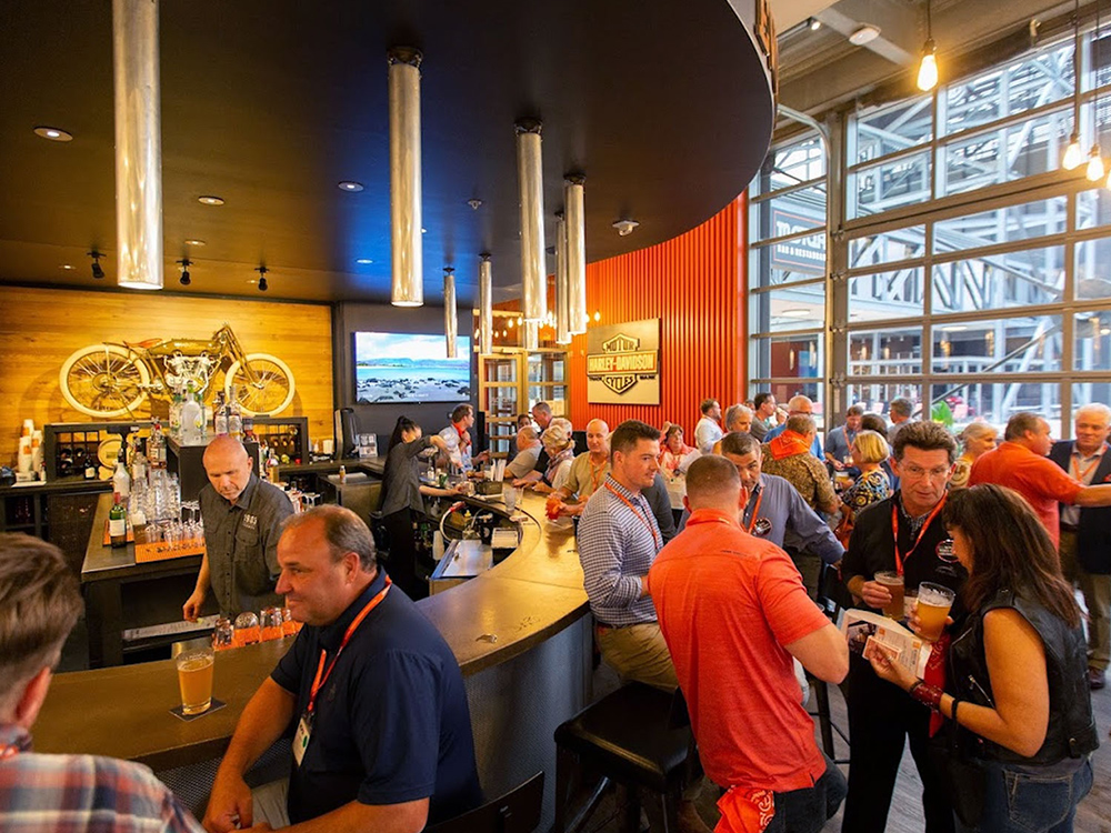 People gathered at Harley-Davidson bar with drinks and motorcycles on display