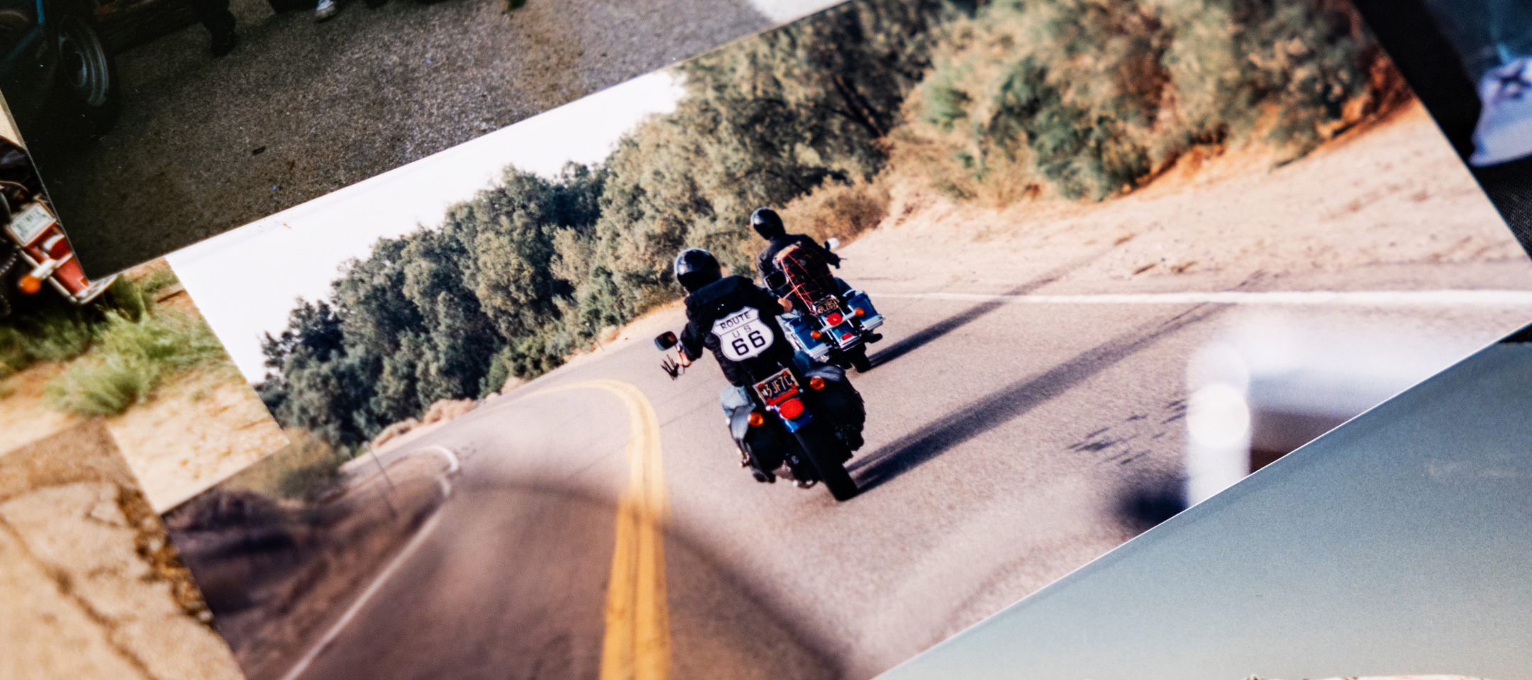 Two riders travel a curving road, one wearing a Route 66 vest, captured from behind in a vintage photo
