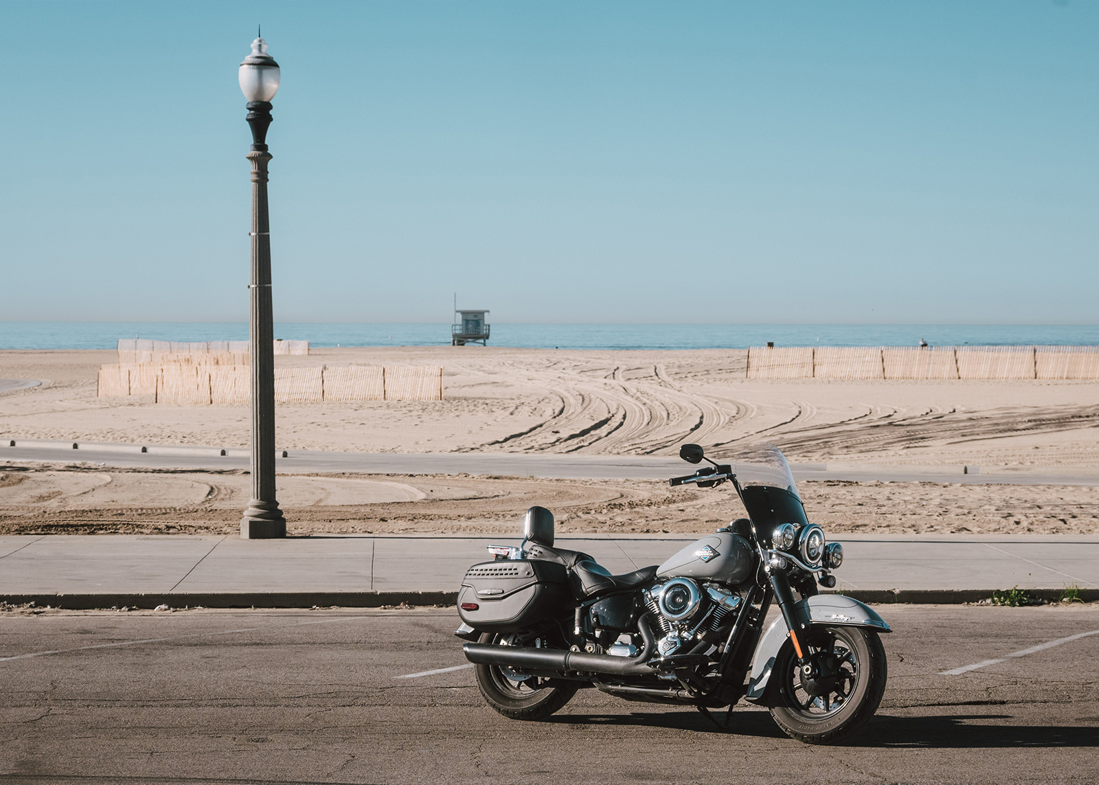  A Harley-Davidson Heritage Classic motorcycle parked near a beachside road with sand dunes, ocean, and a distant lifeguard tower
