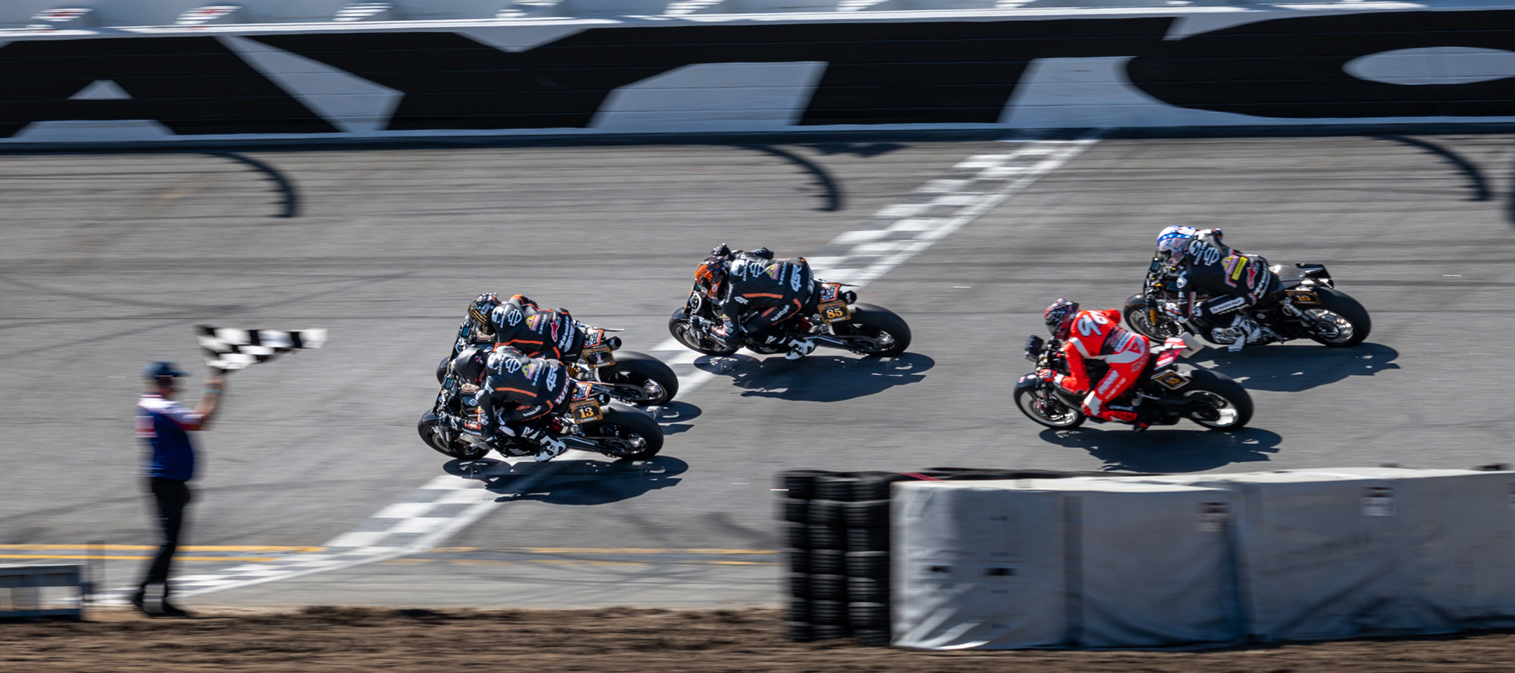 Three Harley-Davidson Super Hooligan motorcycles cross the finish line as an official waves the checkered flag