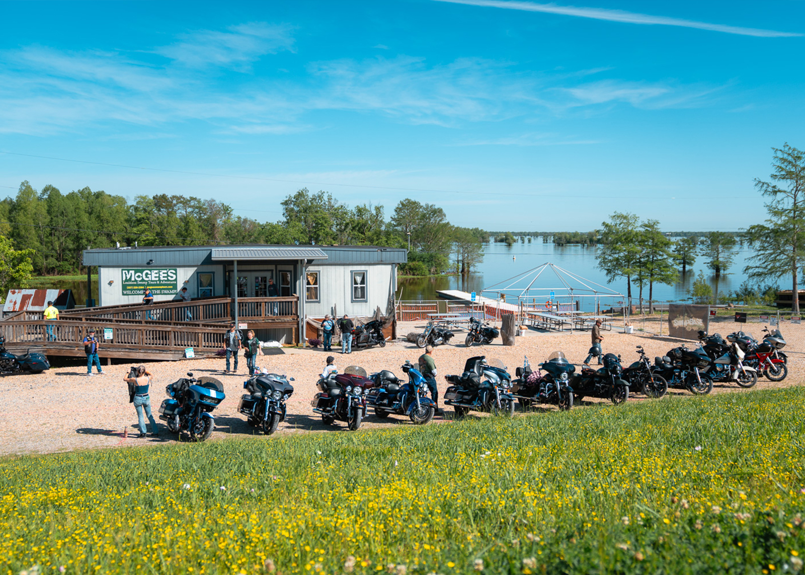 Row of parked motorcycles outside McGee’s landing near a waterfront with trees and clear skies
